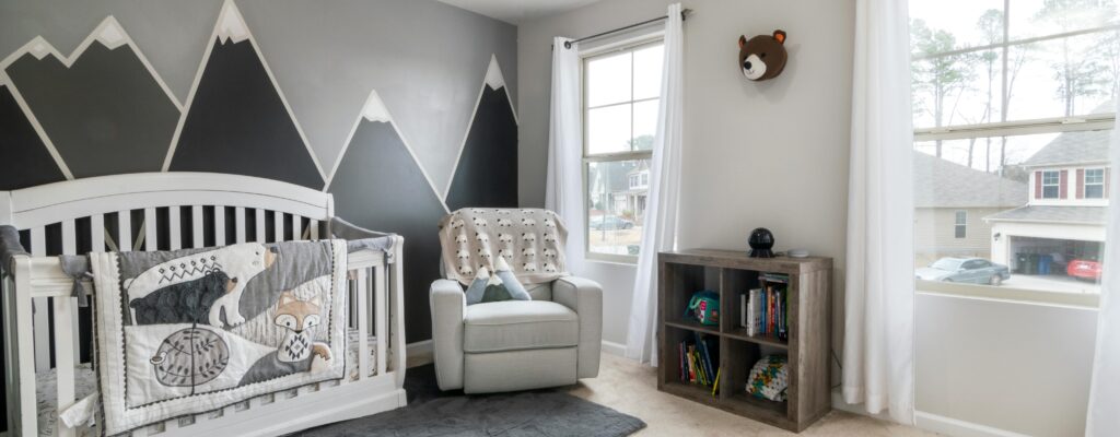 Stylish nursery room featuring mountain mural, comfortable chair, and cozy crib setup.