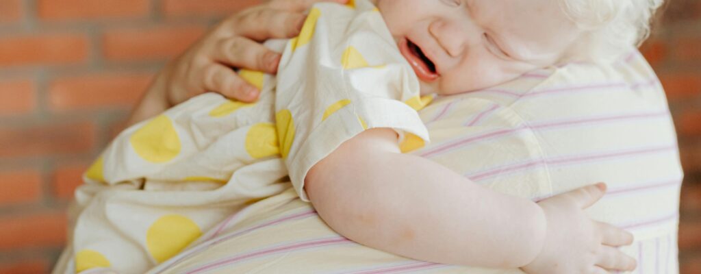 A mother gently holds her crying baby indoors, capturing a tender moment.