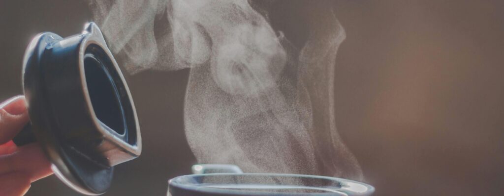 Close-up of steam rising from an open container lid showing hot liquid.