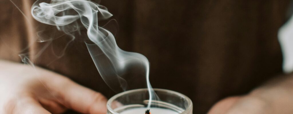 Close-up of hands holding a smoky jar candle with calming ambiance.