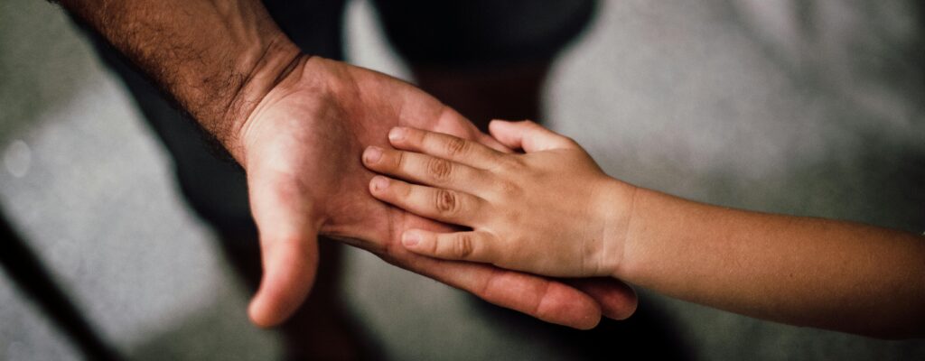 Close-up of a child's hand resting gently on a man's hand, symbolizing love and support.