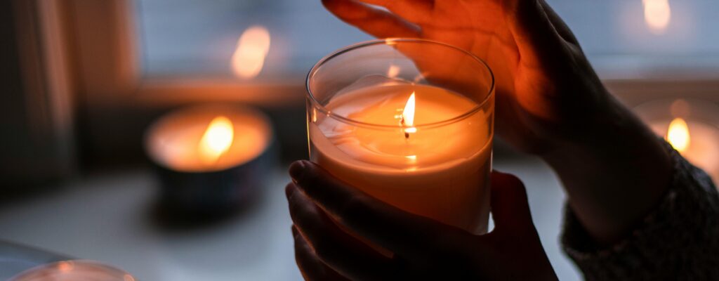 Warm candlelit ambiance with hands gently holding a burning candle indoors.